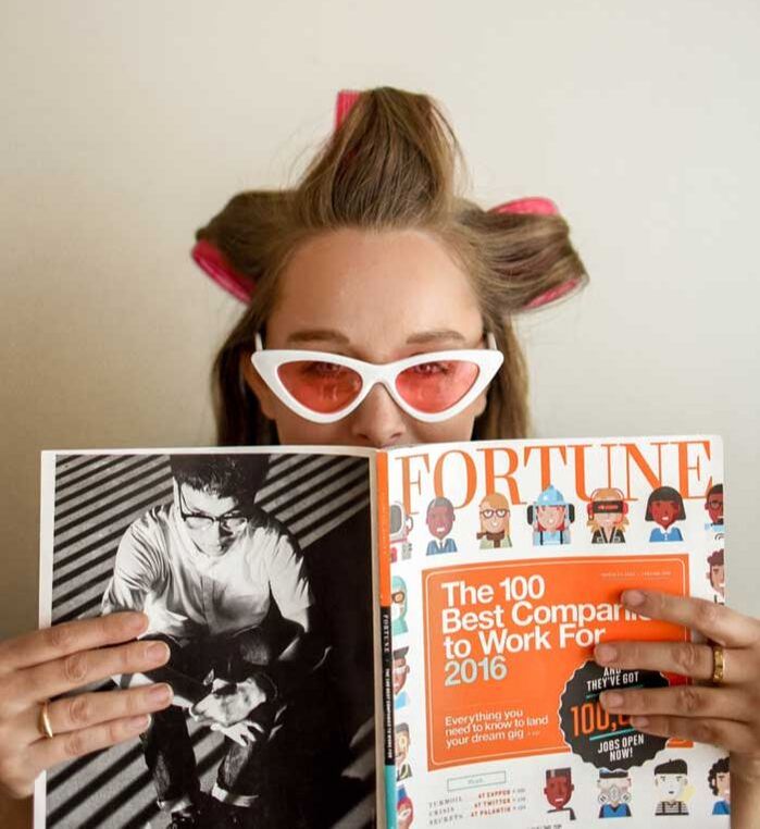 woman at a salon with curlers in her hair reading a magazine